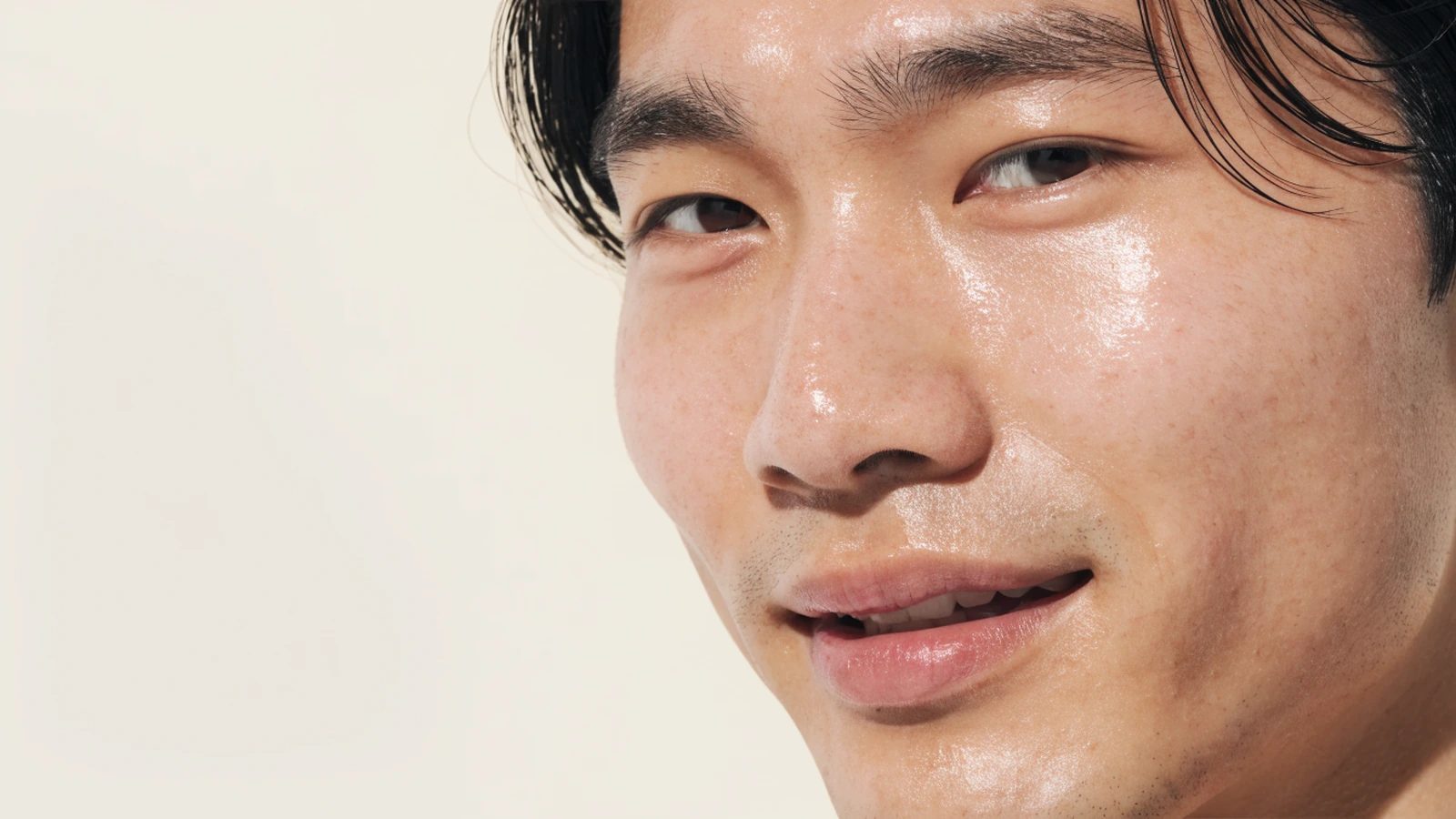 A young man's bare face in soft daylight, natural skin texture with visible pores.