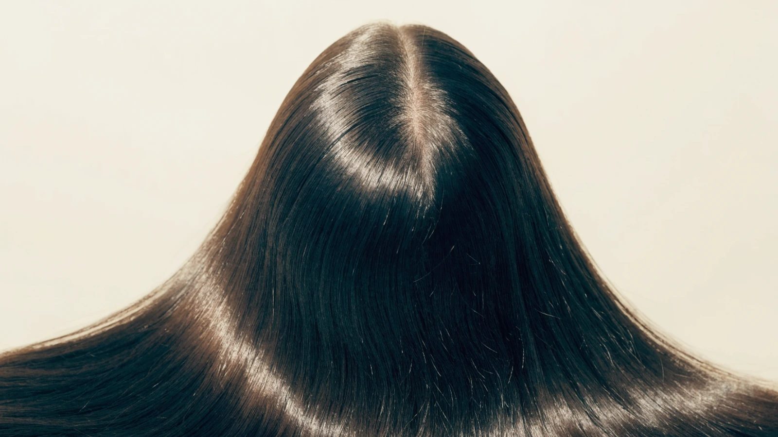 The back of a woman's head, dark hair parted to show the scalp along the parting.