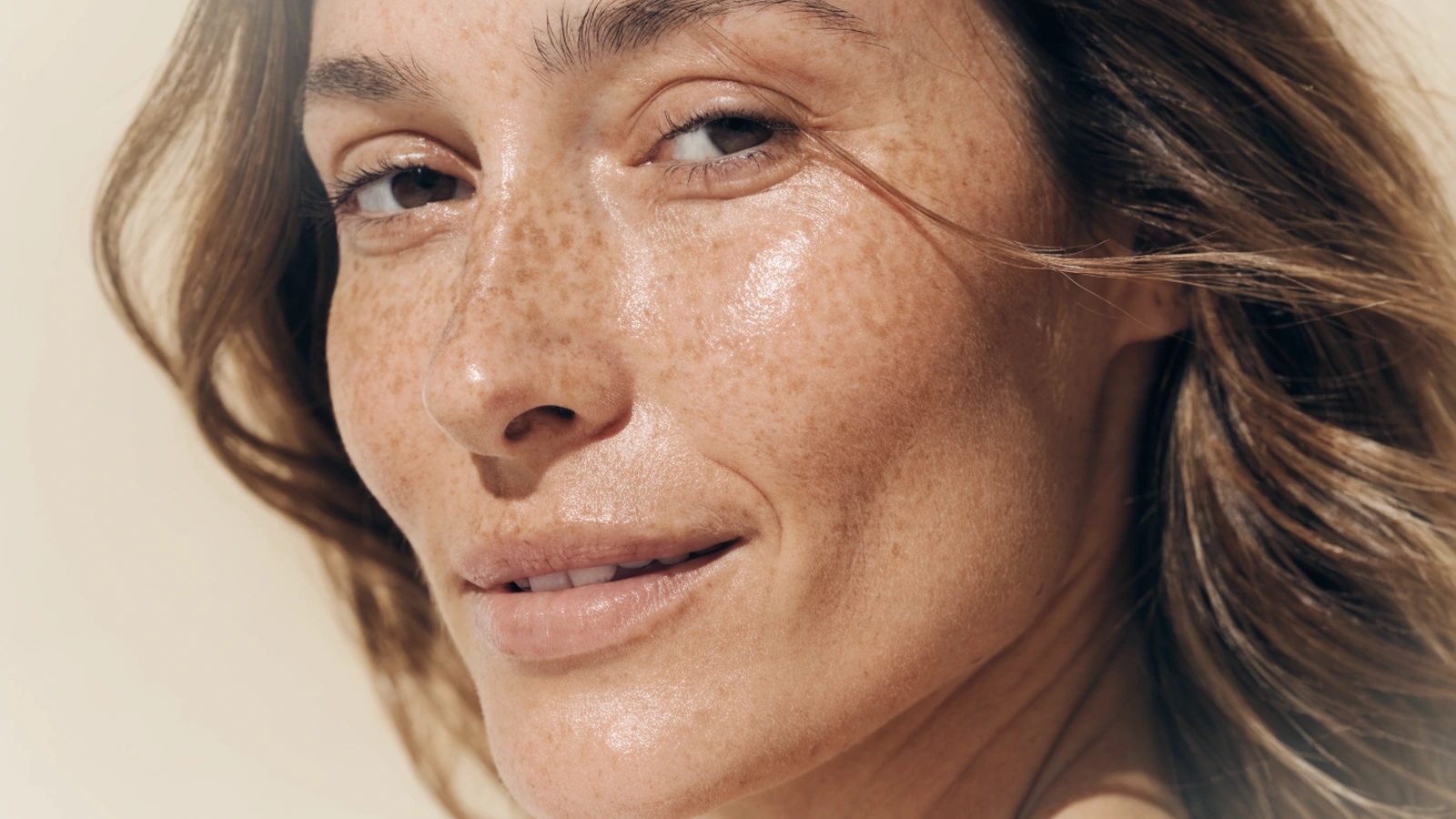 A woman in her thirties, bare face, natural freckling and uneven tone across the cheeks.
