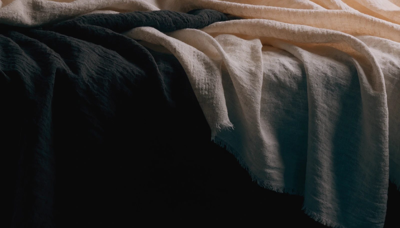 Heavy folds of undyed raw silk and linen in warm raking light.