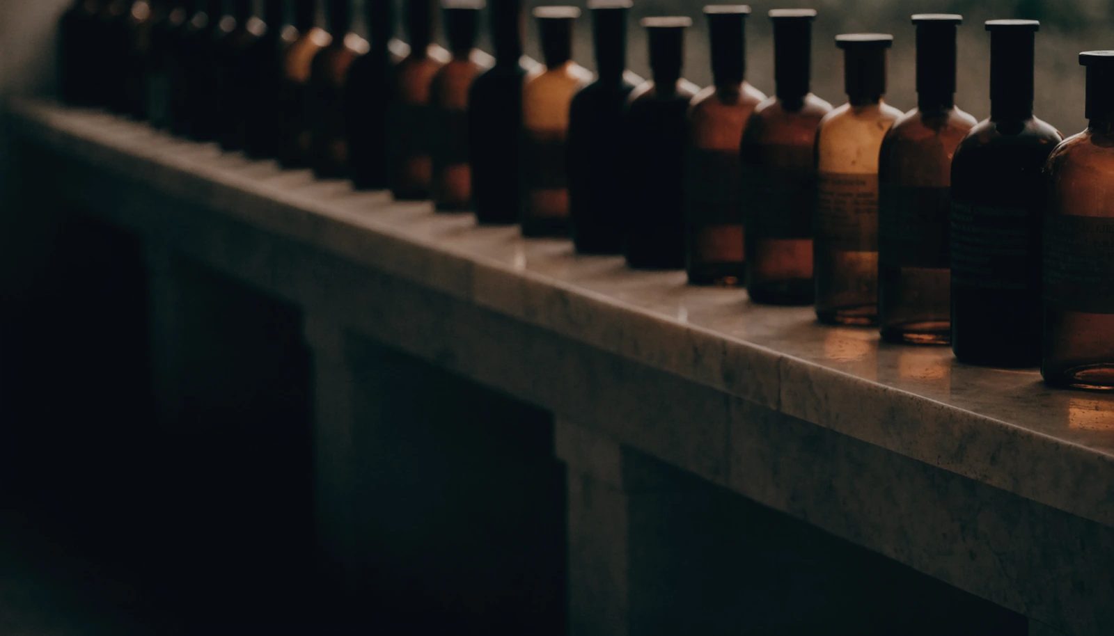 A row of plain amber and smoked-glass bottles on a long stone shelf in a dim apothecary.